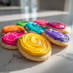 Close-up of sugar cookies topped with bright, colorful, swirled cookie icing in yellow, pink, purple, and blue.