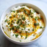 A white bowl filled with creamy whipped goat cheese, drizzled with honey and topped with fresh thyme.