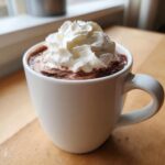 Close-up of rich, dark whipped hot chocolate topped with a generous swirl of fresh whipped cream.