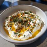 A bowl of creamy whipped ricotta dip drizzled with golden honey, herbs, and chili flakes.