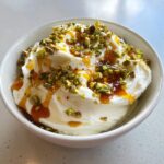 A close-up of creamy whipped ricotta dip topped with chopped pistachios and a drizzle of amber-colored honey.