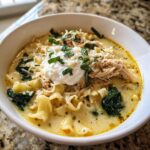 A close-up of a bowl of white chicken lasagna soup topped with shredded chicken, ricotta, and fresh basil.