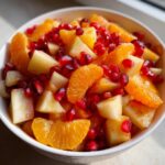 Close-up of a bowl filled with a vibrant winter fruit salad featuring diced apples, orange segments, and pomegranate seeds.