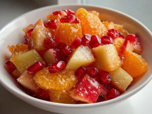 Close-up of a vibrant winter fruit salad featuring orange segments, diced apples, and bright red pomegranate seeds.