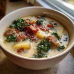 Close-up of a creamy bowl of zuppa toscana soup featuring sausage, potatoes, kale, and bacon crumbles.