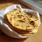 A stack of warm, yellow corn tortillas with charred spots, wrapped in a white cloth.
