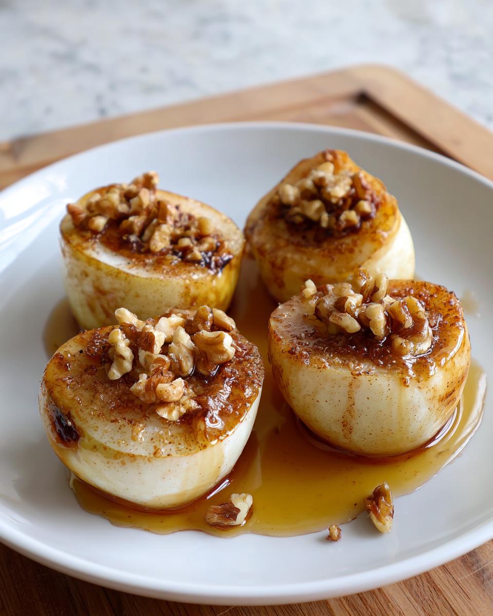 Four halves of warm baked pears drizzled with syrup and topped with chopped walnuts on a white plate.