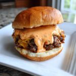 Close-up of a smash burger generously topped with creamy, orange burger sauce, served on a white plate.