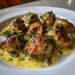 Close-up of several golden-brown chicken piccata meatballs served in a creamy lemon butter sauce, topped with capers and fresh parsley.