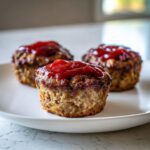 Three perfectly baked mini meatloaf portions topped with a generous dollop of ketchup glaze on a white plate.