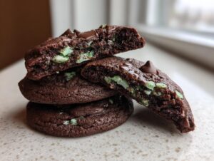 A stack of rich, dark chocolate Andes mint cookies, with one cookie broken in half to show the gooey interior and mint chips.