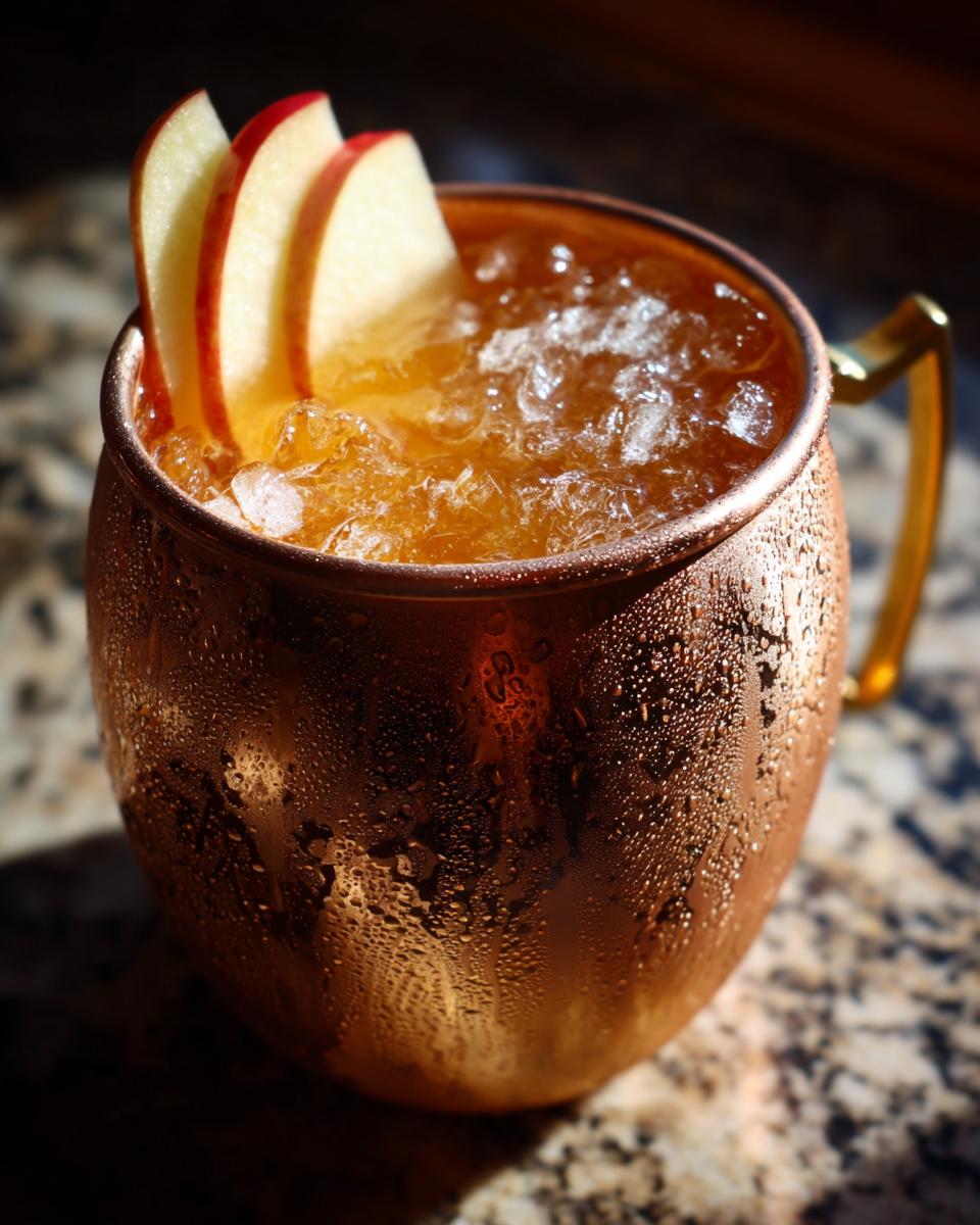 Close-up of a frosty copper mug filled with an apple cider moscow mule, garnished with apple slices.