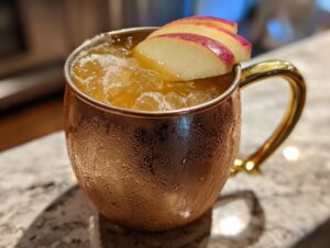 A frosty copper mug filled with an apple cider moscow mule, garnished with thin apple slices.