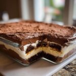 Cross-section view of a rich Baileys Chocolate Cheesecake Trifle showing layers of chocolate cake, cream, and mousse, topped with cocoa powder.