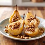 Four halves of glistening baked pears topped with chopped walnuts and syrup, served on a light blue plate.