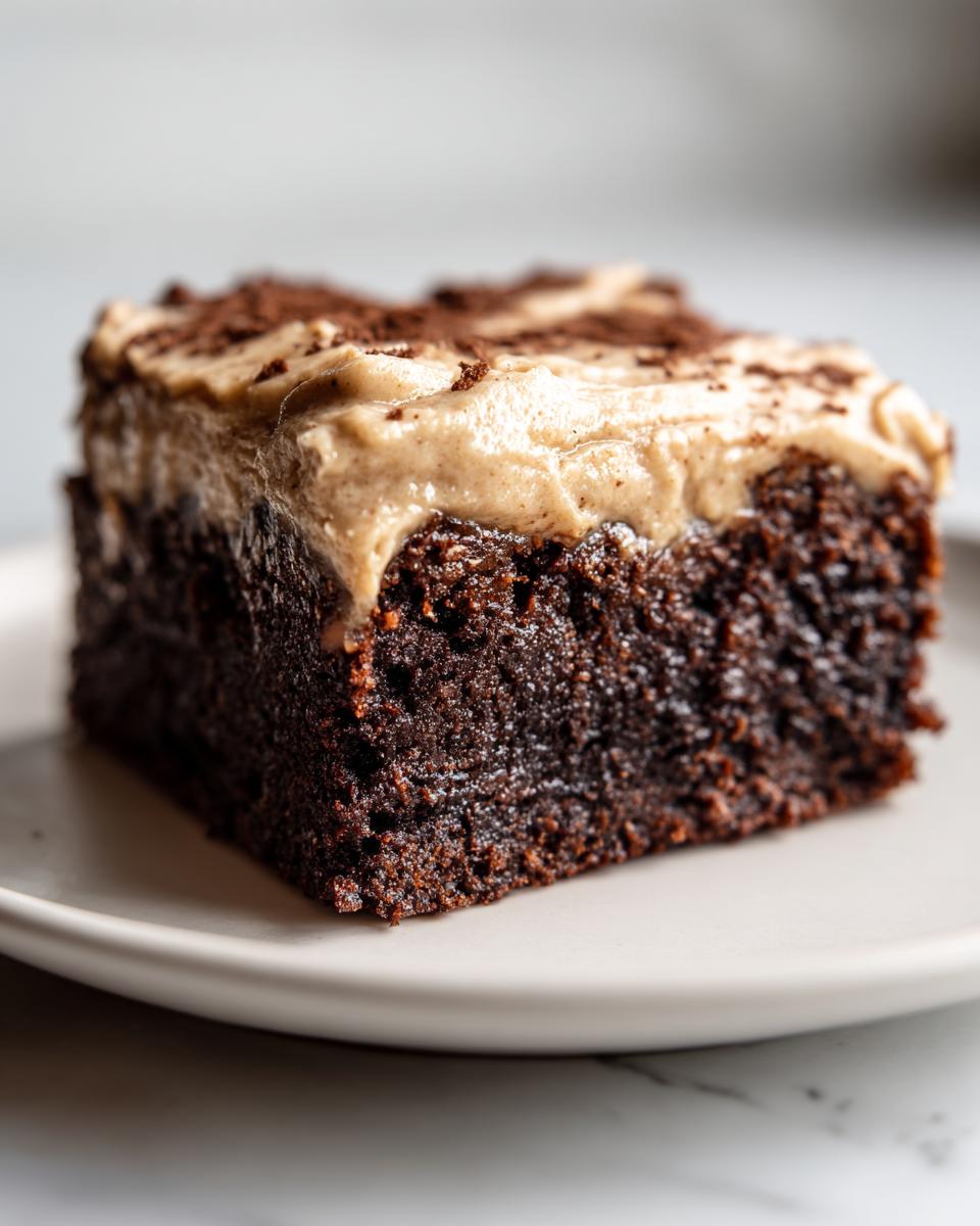 Close-up of a rich, dark chocolate banana bread brownies square topped with light brown frosting and cocoa powder.