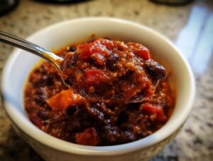 Close-up of a spoonful of rich, thick black bean chili being lifted from a white bowl.