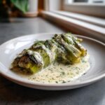 Close-up of tender braised leeks covered in a creamy white sauce and fresh dill.