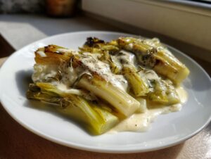 Four pieces of tender braised leeks covered in a creamy sauce and sprinkled with herbs and pepper.