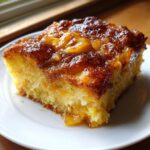 A moist slice of caramel apple dump cake with a glossy, sticky caramel topping and visible apple chunks.