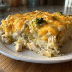 A close-up slice of cheesy chicken and rice casserole topped with melted cheddar and visible pieces of broccoli.