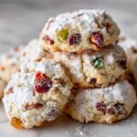 A stack of chewy fruitcake cookies loaded with candied fruit and nuts, heavily dusted with powdered sugar.