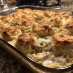 Close-up of a baked chicken pot pie casserole with golden biscuits nestled in creamy filling.