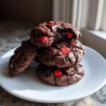 A stack of four rich, dark chocolate cherry cookies featuring bright red cherries and chunks of melted chocolate.