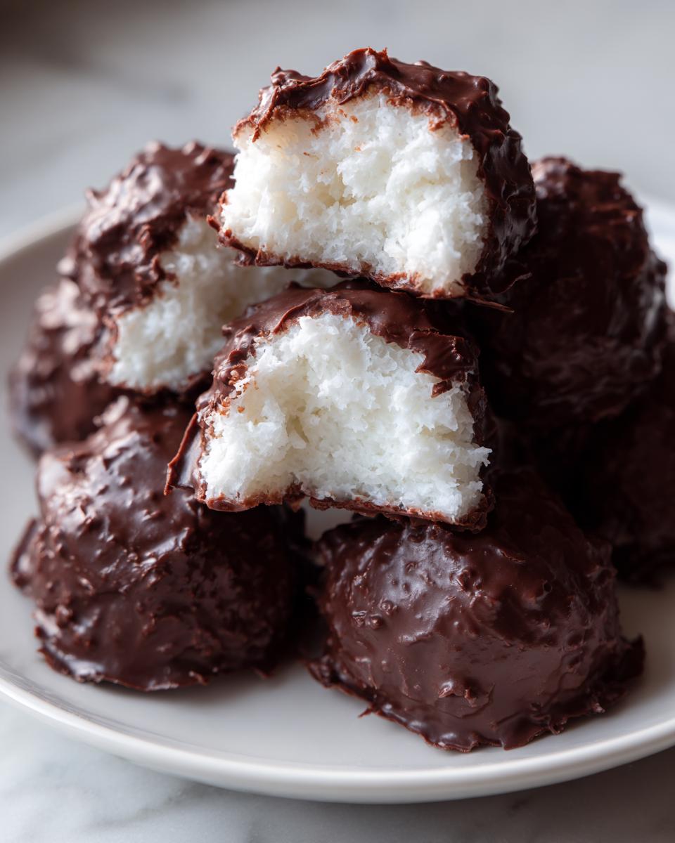 A stack of homemade chocolate-dipped coconut bites, showing the fluffy white interior of the cool whip candy.