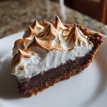 A close-up of a slice of chocolate meringue pie showing the dark chocolate filling and tall, toasted meringue topping.