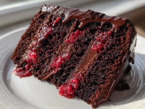 Close-up of a moist slice of chocolate raspberry cake showing dark layers, raspberry filling, and chocolate ganache dripping down the side.