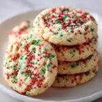 A stack of soft, round christmas sprinkle sugar cookies topped with festive red, green, and white sprinkles.