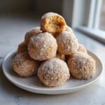 A stack of freshly made cinnamon sugar snowball cookies heavily coated in sparkling sugar, with one cookie broken open on top.
