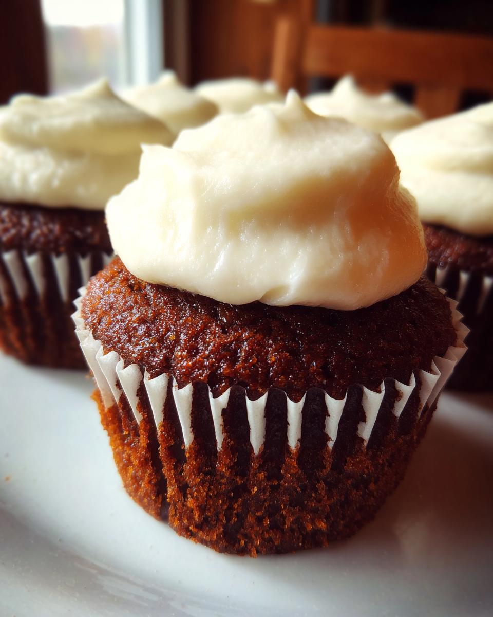 A close-up of a rich, dark brown gingerbread cupcake topped with thick, creamy white frosting.