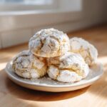 A stack of four soft, cracked cool whip cookies heavily dusted with powdered sugar, sitting on a small white plate.
