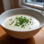 A close-up of a bowl of creamy white cauliflower soup topped generously with chopped green chives.