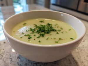 Close-up of a bowl of creamy celery soup, garnished with chopped fresh parsley and pepper.