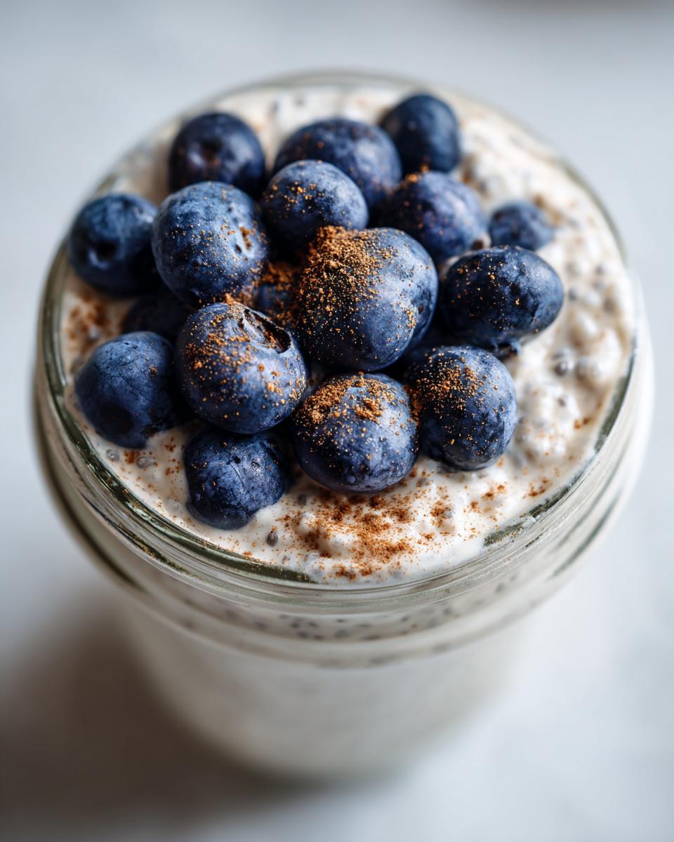 Overhead close-up of creamy chia seed pudding in a glass jar, topped with fresh blueberries and a dusting of cinnamon.