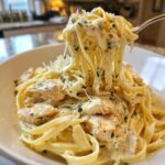 A fork lifting a generous twirl of creamy chicken fettuccine alfredo pasta from a white bowl.