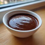 A close-up of rich, dark chocolate pudding served in a small white bowl on a wooden surface.