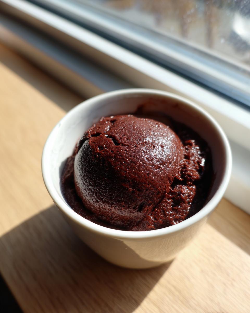 A perfectly scooped portion of rich, dark chocolate pudding in a white bowl.