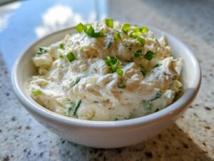 Close-up of creamy clam dip in a white bowl, garnished with fresh chopped green chives.