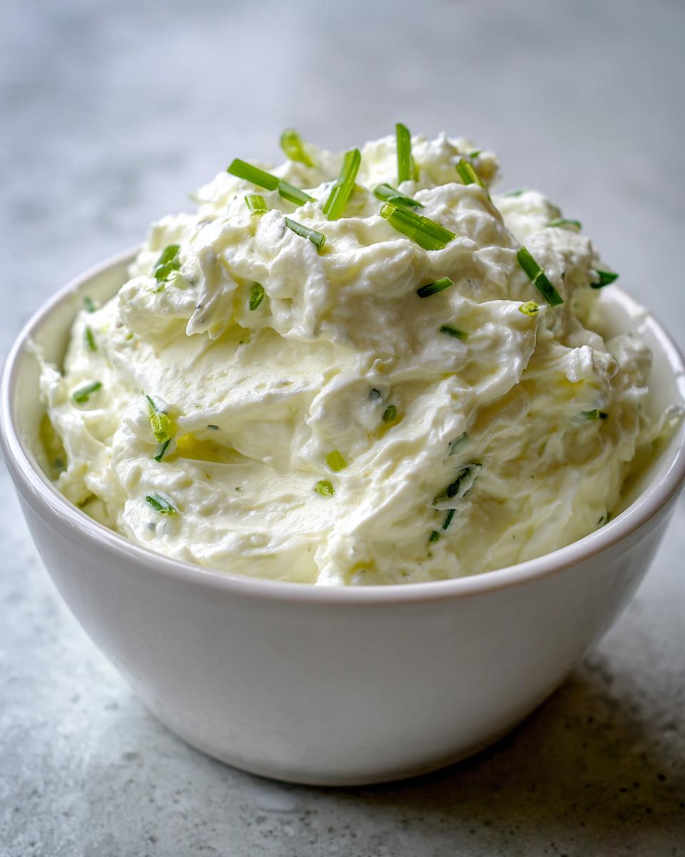 A close-up of a white bowl filled with creamy clam dip, garnished generously with bright green chopped chives.