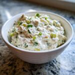 A white bowl filled with creamy clam dip, garnished generously with chopped green onions.