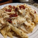 Close-up of creamy crockpot marry me chicken served over penne pasta, topped with sun-dried tomatoes and herbs.