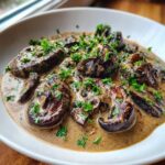 Close-up of rich, creamy mushroom sauce covering whole and sliced mushrooms, garnished with fresh parsley.