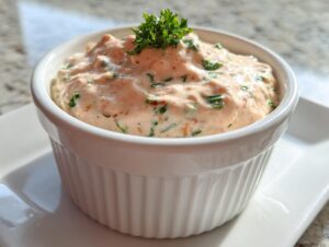 A creamy, pinkish-orange remoulade sauce garnished with fresh parsley in a small white fluted ramekin.