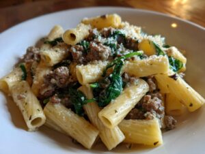 Close-up of creamy sausage pasta featuring rigatoni, crumbled sausage, wilted spinach, and grated parmesan cheese.