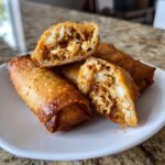 Close-up of golden brown, crispy fried egg roll cut in half, revealing a savory shredded filling.
