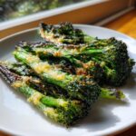 Close-up of perfectly charred and crispy smashed broccoli topped with melted cheese on a white plate.
